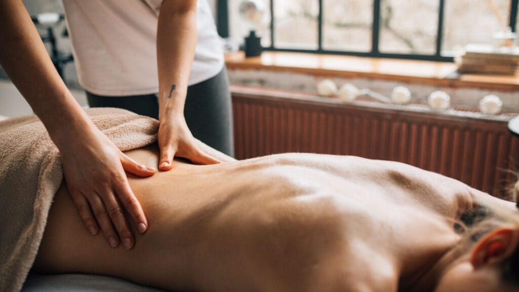 Fizjoterapeuta wykonuje masaż pleców pacjenta leżącego na kozetce